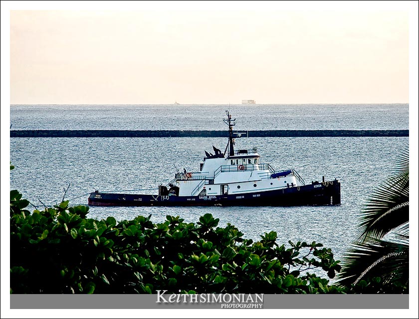A tug boat passes near the coastline by the city of Hilo on the Big Island of Hawaii.