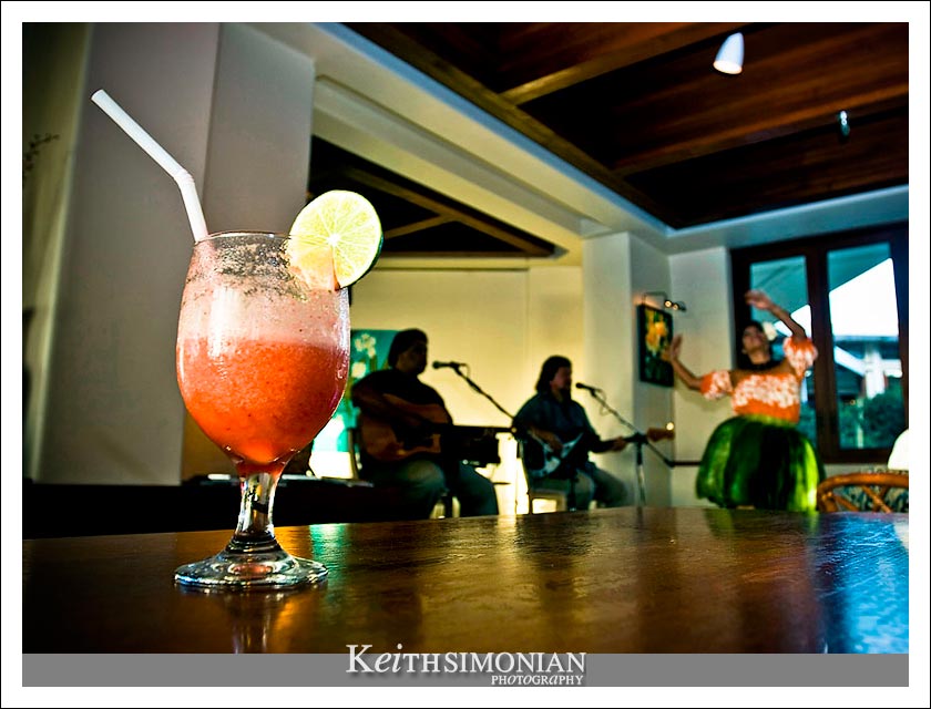 16-May-2005: Maui, Hawaii. A Hula girls dances in the background with a tropical drink in the foreground at a bar in the Maui Prince Hotel.