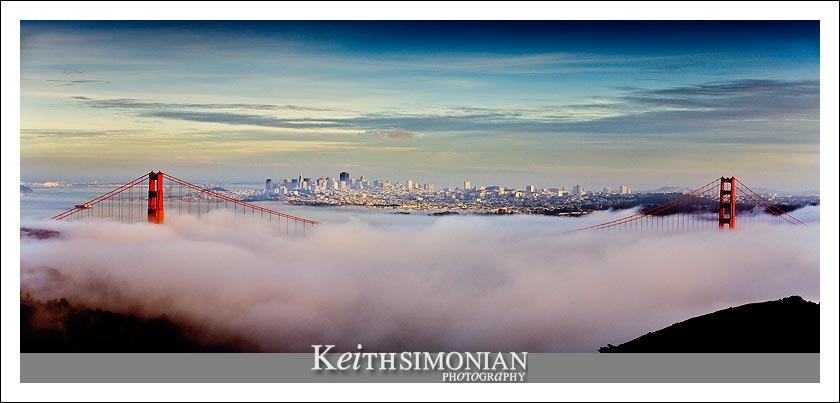 Fog covers the base of the Golden Gate Bridge with San Francisco skyline in the background of this photo