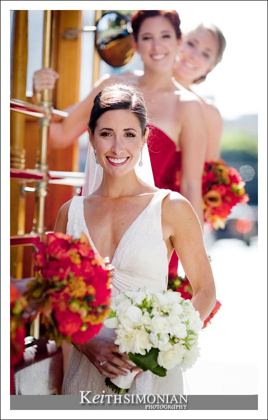 Bride on the side of cable car with her bridesmaids in red dresses