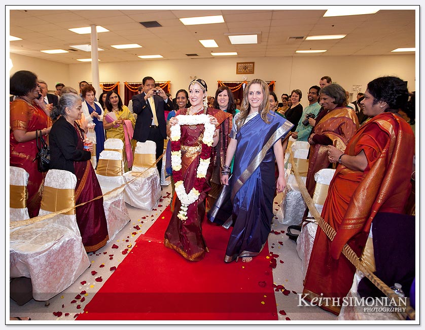 The bride carrying a red and white garland for the groom walks on the red carpet at the Shiva-vishnu Temple in Livermore, CA