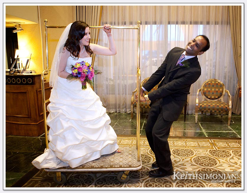 The bride and groom have a little fun with the hotel's luggage cart at the Newark/Fremont Hilton Hotel