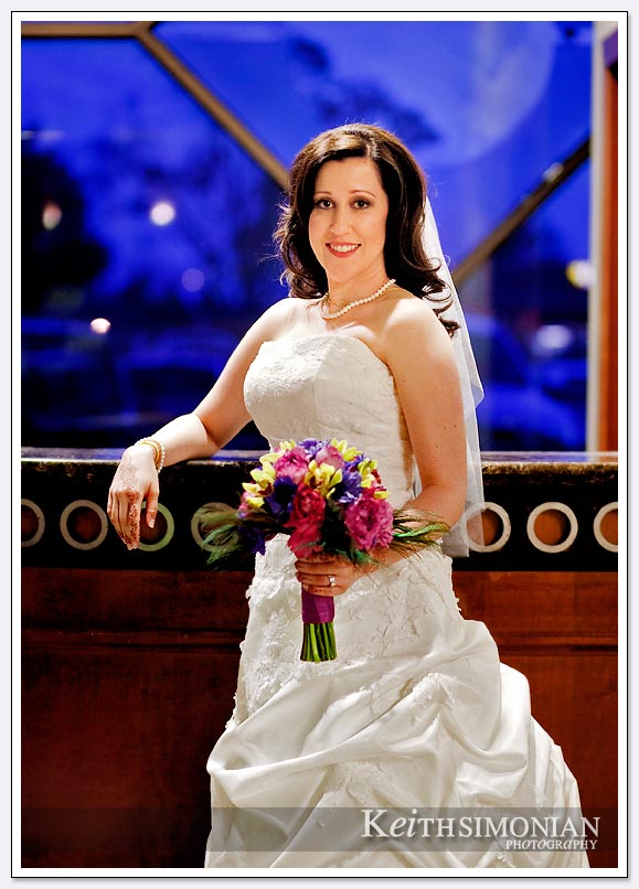 The bride poses for a formal portrait in front of a blue window with her bouquet at the Fremont/Newark Hotel