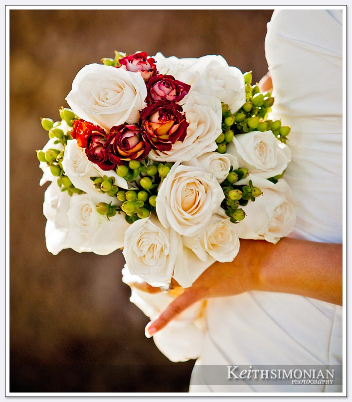 The bride holds her bouquet which has red and white flowers