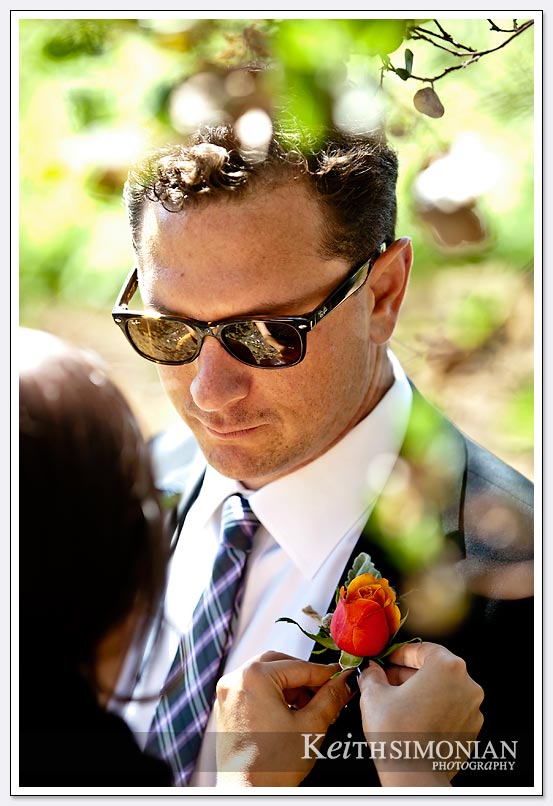 The greenery of a Napa Valley vineyard frame this photo of groomsman getting flower pinned on