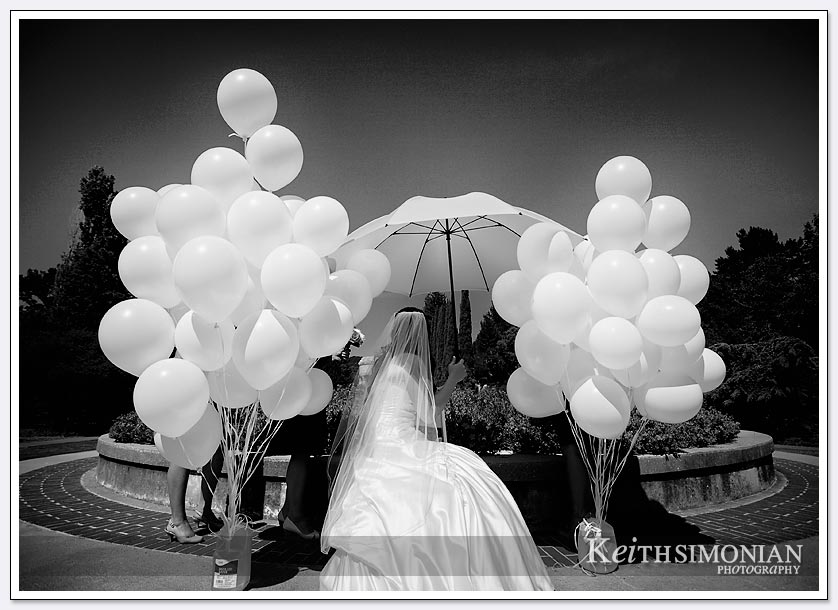 The bride waits under the umbrella surrounded by the white balloons the will be released at the end of wedding ceremony