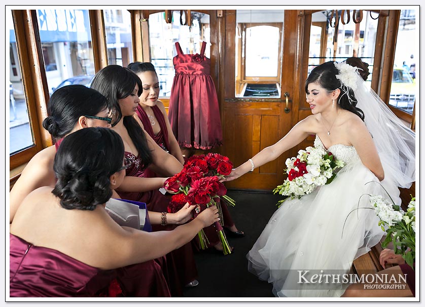 Bride with bridesmaids in red dresses ride trolley to St. Ignatius church in San Francisco.