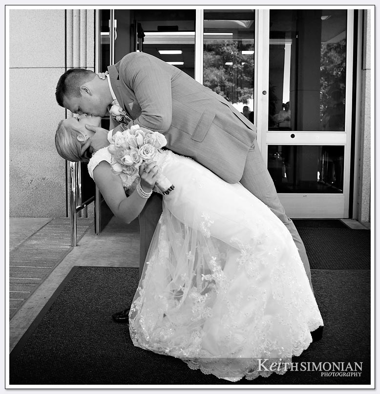 The groom dips the bride and kisses her outside the Oakland LDS temple