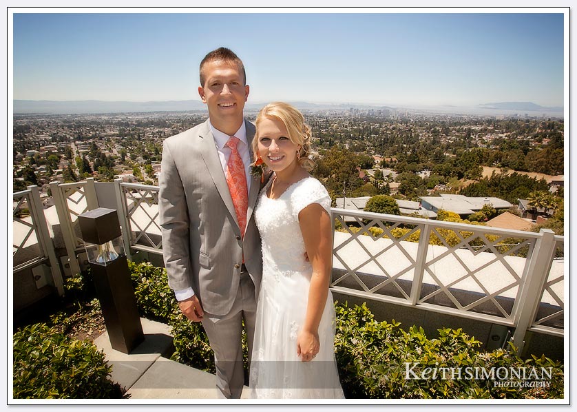 The bride and groom pose with the San Francisco Bay area in the background outside the Oakland LDS temple