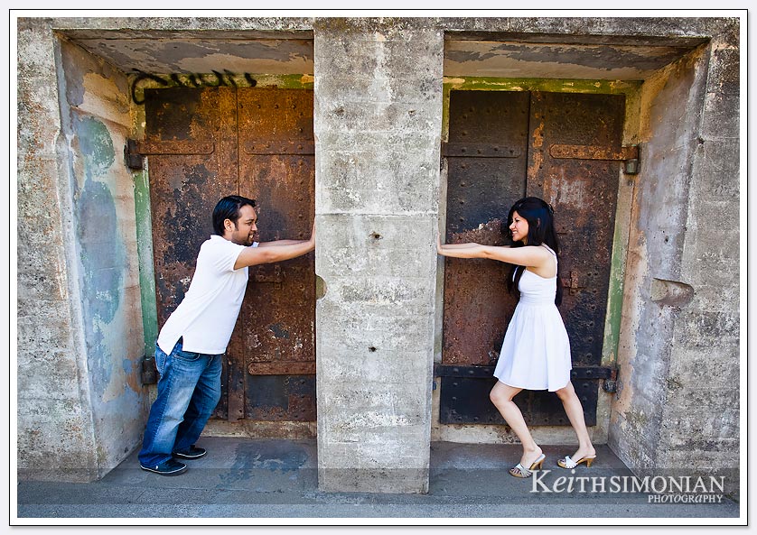 The couple tries to push the stone wall towards each other - San-Francisco-Engagement-Photos