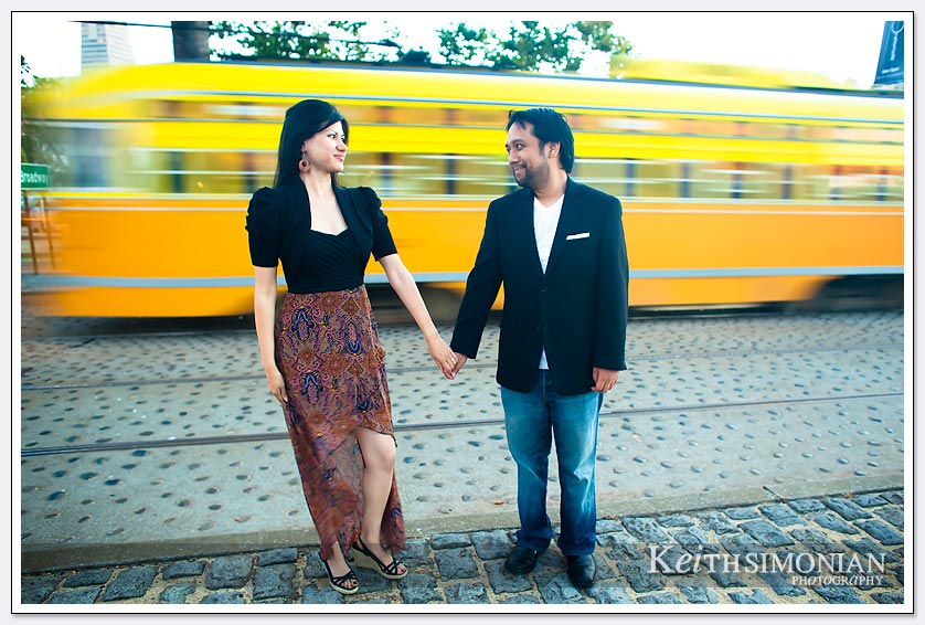 The couple holds as the yellow vintage Muni trolley car zooms by - San-Francisco-Engagement-Photos