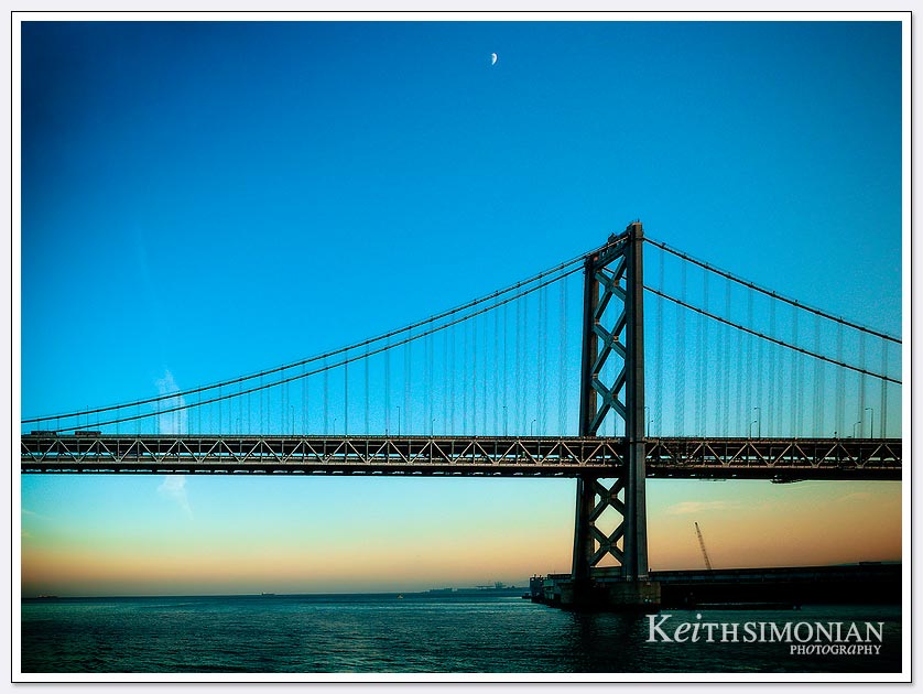 The moon rising over a sunset view of the Bay Bridge