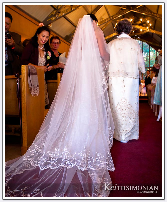 The bride walks up the aisle as her veil trails her