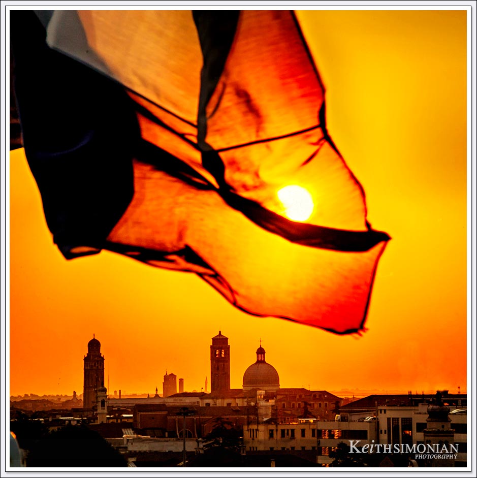 The ship's flag covers the sun as it rises over Venice, Italy.