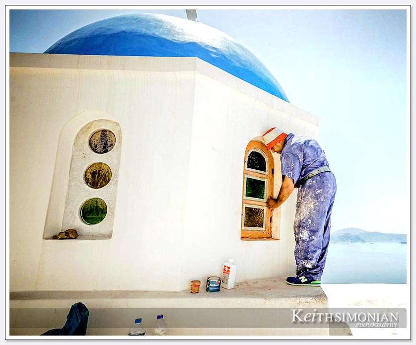 Worker painting some of the buildings white on Santorini, Greece