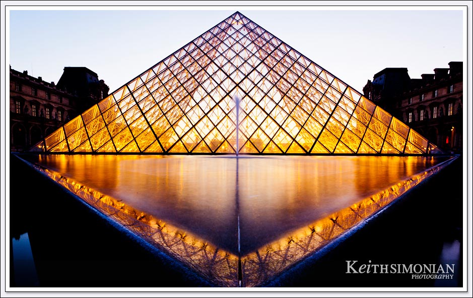 The reflection pond and the glass pyramid in the courtyard of the Louvre Museum at night - Paris France.