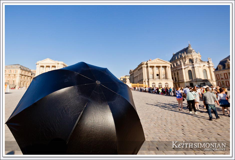 The line of visitors waiting to enter the Palace of Versailles can be quite long and this visitor took shade under a black umbrella.