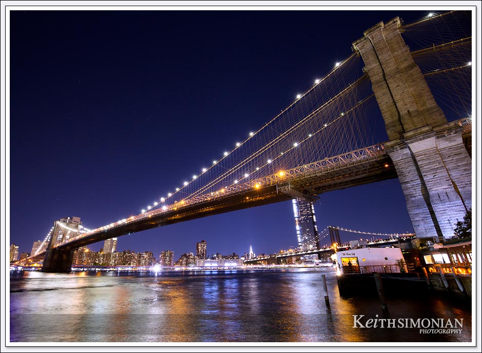 The night lights reflect off the East river as the Brooklyn bridge stands above.