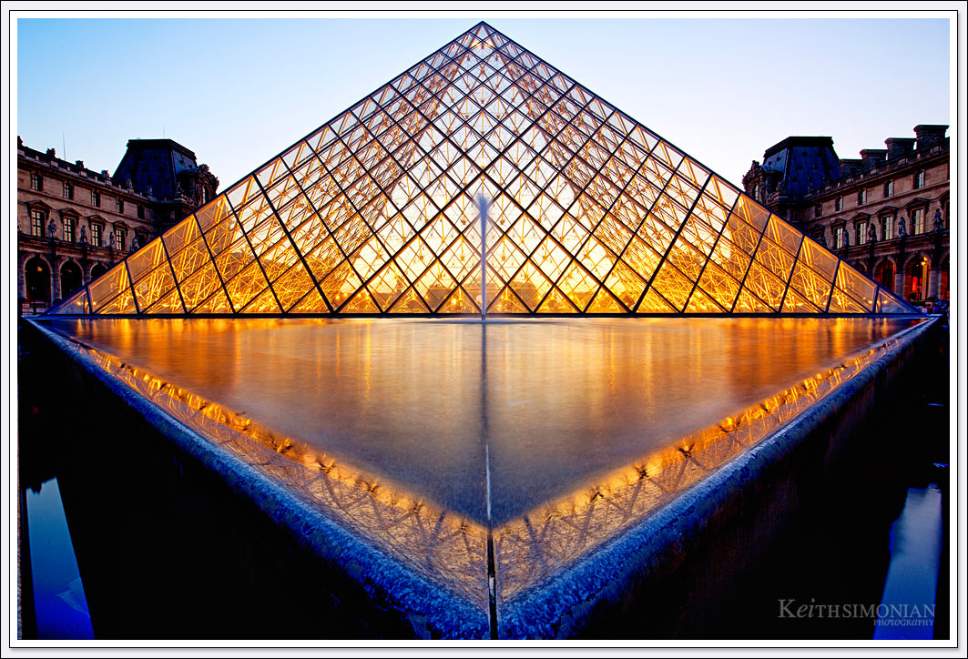 The reflection pond and the glass pyramid designed by I. M. Pei lit up during twilight at the Louvre Museum in Paris France.