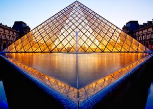 The glass pyramid designed by I. M. Pei lit up during twilight at the Louvre Museum in Paris France.