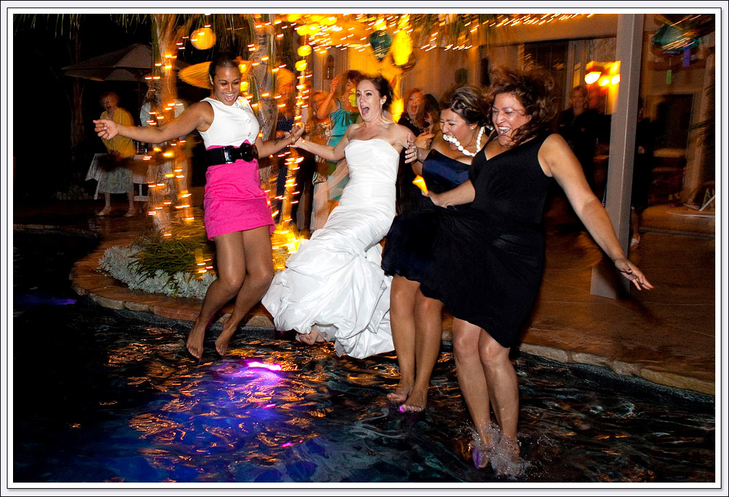 Bride and bridesmaids trashing their dresses by jumping into the swimming pool at this backyard wedding reception. 