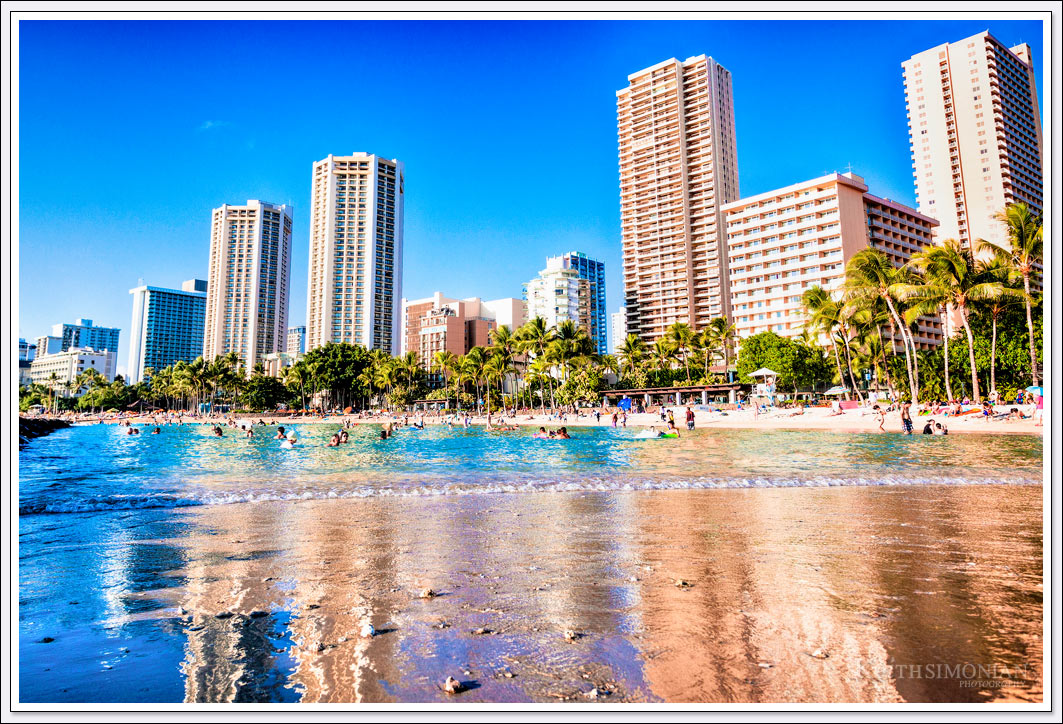 Some of the many hotels along Waikiki Beach reflect in the calm beach water